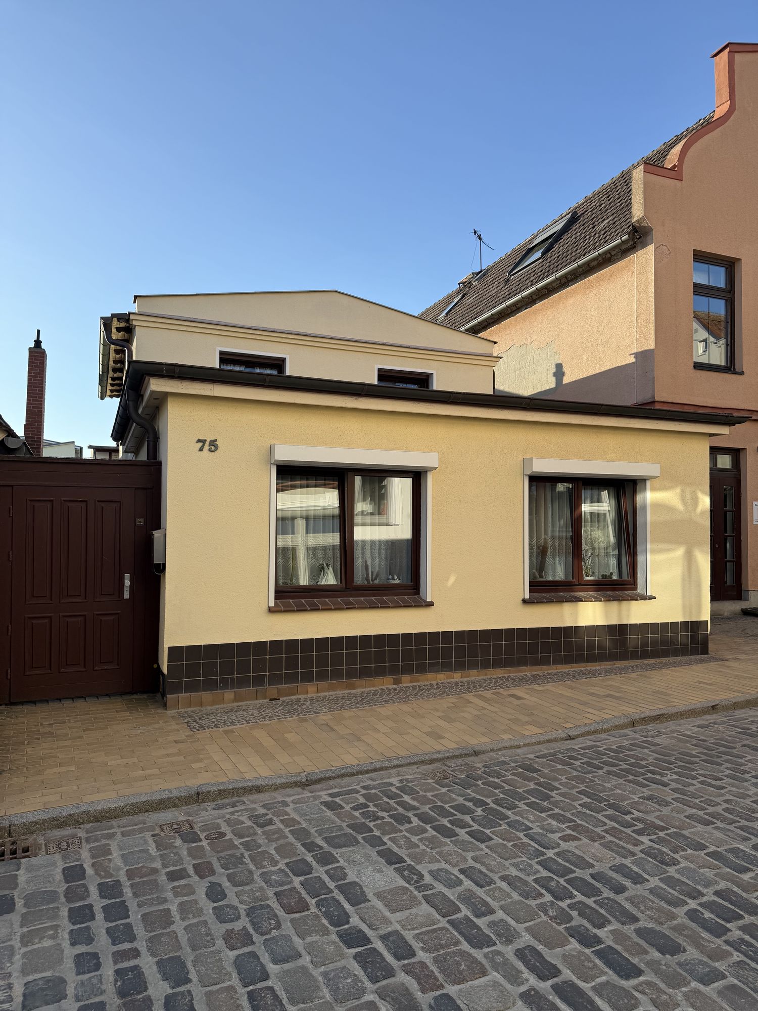 Vorderhaus der Alexandrinenstraße 75 mit Hausnummer, sandfarbene Fassade, Kopfsteinpflasterstraße